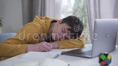 聪明的白种人十几岁的男孩睡着了，在工作簿上写作。 努力学习的疲惫大学生的画像